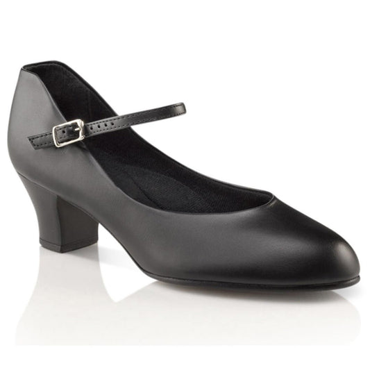 Capezio Jr. Footlight character shoe on model in black/caramel PU upper, with 1.5″ non‑slip plastic heel topped with leather lift, slim buckle closure, and closed-toe design.