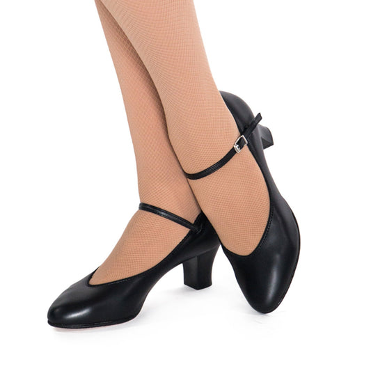 On‑foot view of black ‘S’ Broadway shoe worn with hosiery, featuring secure T‑strap fit, curved heel, and polished silhouette for stage ensemble wear